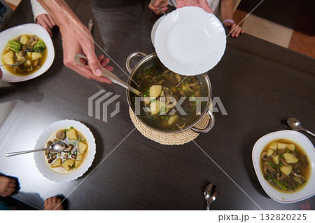 Father Cooking Soup for Family Dinner: Hands Ladling Broth While Children Eat at the Table 132820225