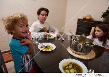 Family Dinner: Three Kids At The Kitchen Table Sharing Soup From A Pot Family Dinner: Three Kids At The Kitchen Table Sharing Soup From A Pot 132820229
