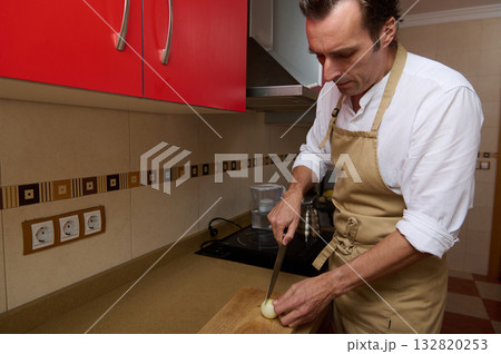 Man Cooking Onion In Apron In Modern Kitchen, Chopping Onions For Dinner 132820253