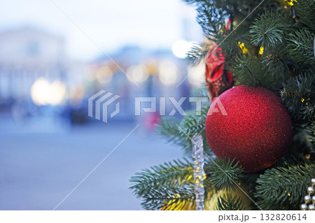 Red ball on Christmas tree on background of city street. Street is out of focus. Place for advertising. Background for Christmas card. Red ball on Christmas tree on background of city street. Street is out of focus. Place for advertising. Background for Christmas card. 132820614