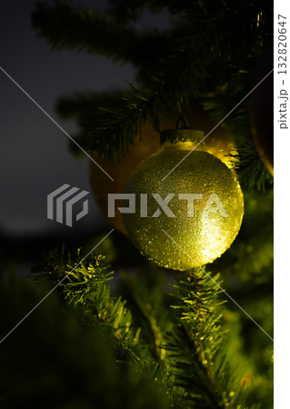 A shiny golden Christmas tree ball against a dark background. The glittery ball is covered with frozen raindrops. A template for an atmospheric New Year's card. Vertical image, close-up, copy space. 132820647