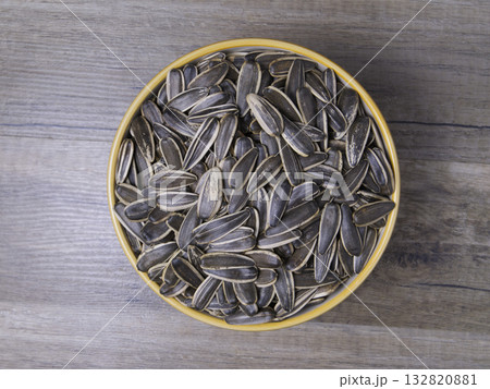 Striped sunflower seeds in a bowl on a wooden table. 132820881
