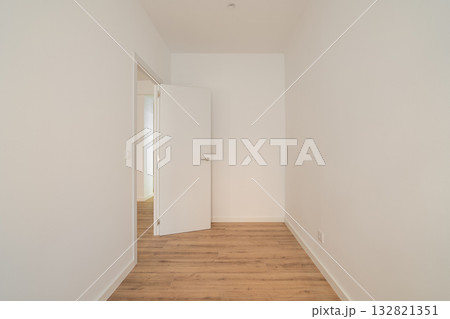 Empty room with white walls and wooden floor. A door is slightly open, leading to another space. The room is well-lit and minimalistic. 132821351