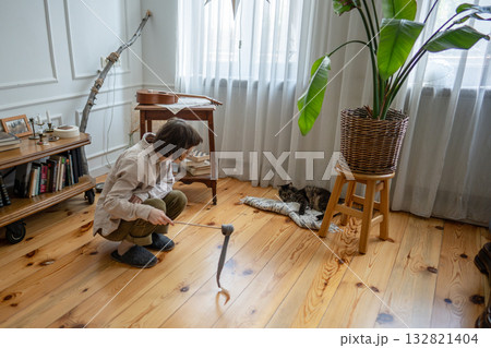 Young woman activating lazy cat on floor. Playful stimulation for healthy feline instinct play 132821404