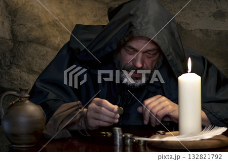 A medieval monk counting coins by candlelight. 132821792
