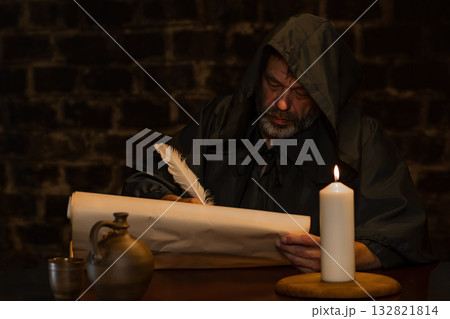 A medieval monk writes with a quill pen on parchment by candlelight. A medieval monk writes with a quill pen on parchment by candlelight. 132821814