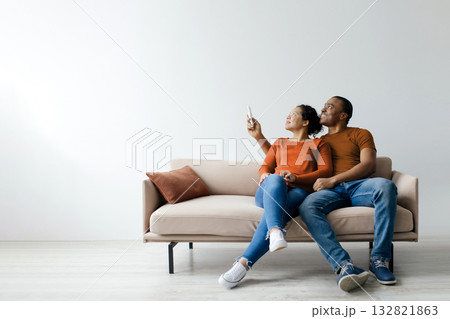 Split system. Cheerful young black couple opening air conditioner with remote 132821863
