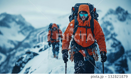 Two climbers are climbing up a snow-covered mountain slope. They are using trekking poles and carrying backpacks. The weather is harsh and snowy, but the climbers are focused on their journey. 132821879