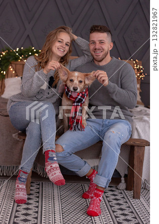 Happy Couple and Dog Enjoy Festive Winter Christmas Moments Together. The image celebrates love, joy and the warmth of the holiday season at cozy home. 132821967