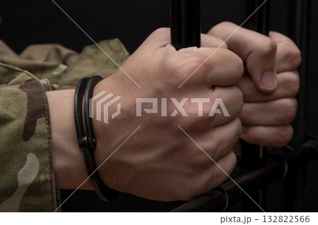 Handcuffed soldier clutching the bars with his hands against a black background. Concept: trial of a soldier, desertion in the army, prisoner of war. 132822566