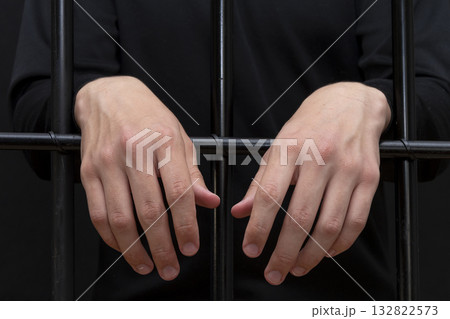 The convicted man hung his hands on the bars in the courtroom, dark tone, selective focus. 132822573
