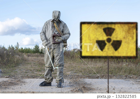 A military man in chemical protection and a gas mask measures the radiation level with a dosimeter, a radiation hazard sign, a concept: radiation leakage, the threat of infection. 132822585