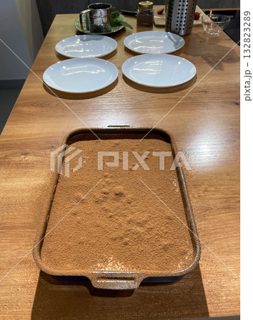 Homemade tiramisu dessert on wooden table before serving. Culinary preparation, comfort food, and cozy home atmosphere. Homemade tiramisu dessert on wooden table before serving. Culinary preparation, comfort food, and cozy home atmosphere. 132823289