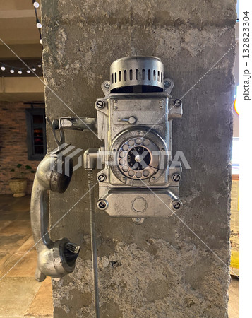 Retro rotary telephone mounted on raw concrete surface in dimly lit interior. Industrial heritage, nostalgia, and communication history concept. 132823304