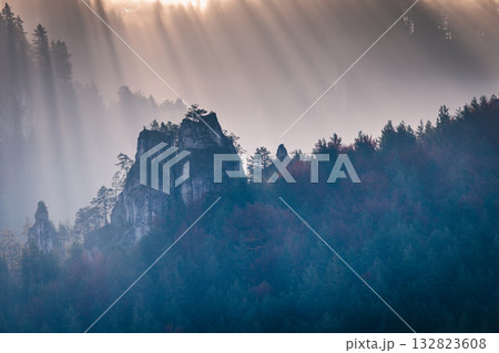 Sunbeams pierce through fog, illuminating a rocky outcrop amidst a dense forest. Serene, majestic, and bathed in ethereal light. The Mala Fatra national park in Slovakia, Europe. Sunbeams pierce through fog, illuminating a rocky outcrop amidst a dense forest. Serene, majestic, and bathed in ethereal light. The Mala Fatra national park in Slovakia, Europe. 132823608