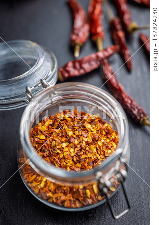 Red chili peppers flakes. Milled spicy peppers in jar on black table. 132824230