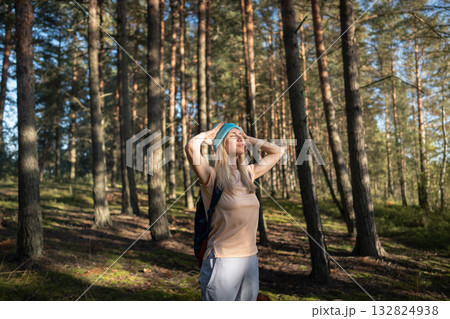 Serene female meditating hands behind head taking deep breaths with closed eyes under forest sun Serene female meditating hands behind head taking deep breaths with closed eyes under forest sun 132824938