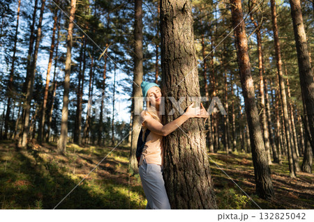 Calm woman standing in forest and hugging big tree trunk at sunset, loving nature, relieving stress 132825042