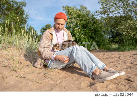 Man pet owner spending time outdoor with dissatisfied scared cat, sits on beach cost with pet on lap Man pet owner spending time outdoor with dissatisfied scared cat, sits on beach cost with pet on lap 132825044