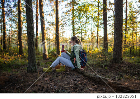 Female hiker taking break after walk in forest and forage, sitting on log drinking water from bottle Female hiker taking break after walk in forest and forage, sitting on log drinking water from bottle 132825051