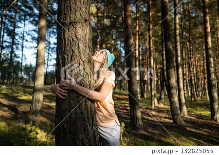 Satisfied woman hugging tree trunk while look up into canopy in quiet forest. Mindfulness in nature Satisfied woman hugging tree trunk while look up into canopy in quiet forest. Mindfulness in nature 132825055