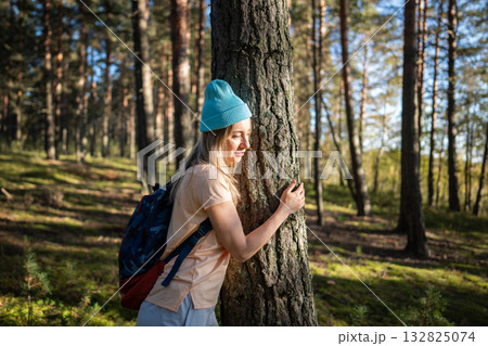 Smiling serene woman embracing tree in forest. Adventurer in woods, sustainable living with nature Smiling serene woman embracing tree in forest. Adventurer in woods, sustainable living with nature 132825074