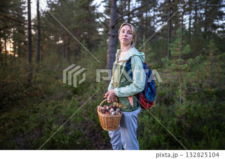 Female forager explorer stand in autumn woodland with basket full of wild boletus mushrooms in hand. Female forager explorer stand in autumn woodland with basket full of wild boletus mushrooms in hand. 132825104