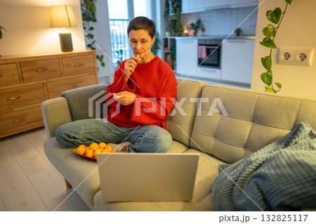 Relaxed mature woman watching movie. Content female eating mandarin laptop sofa, Downtime with snack 132825117