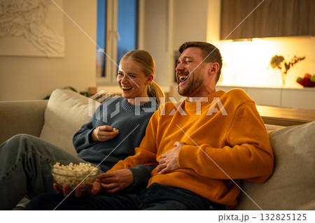 Family movie night, young couple laughing and eating popcorn while watching comedy at cozy home 132825125