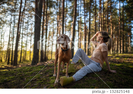 Relaxed carefree woman resting in forest lawn with dog at sunset. Satisfied female hiker rest Relaxed carefree woman resting in forest lawn with dog at sunset. Satisfied female hiker rest 132825148