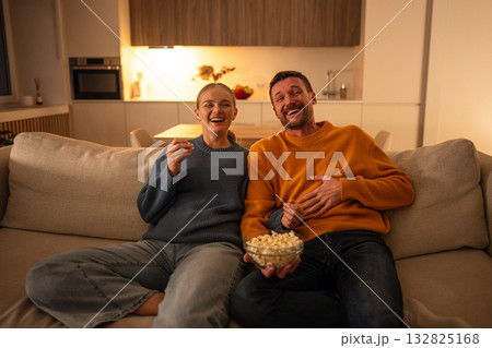 Happy intrigued couple watching movie with popcorn at home cozy together enjoying shared tradition 132825168