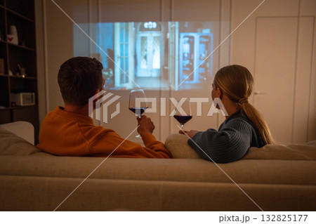 Couple enjoying romantic evening with wine and movie projected on screen at home on sofa rearview 132825177