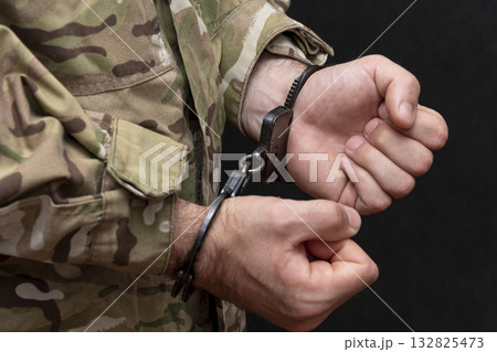 A soldier in a military camouflage uniform is handcuffed on a black background. A soldier in a military camouflage uniform is handcuffed on a black background. 132825473