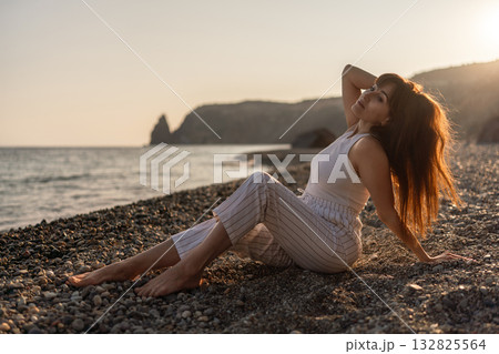 Woman beach sunset. Young woman relaxing on pebble beach at golden hour, enjoying the peaceful nature and warm light Woman beach sunset. Young woman relaxing on pebble beach at golden hour, enjoying the peaceful nature and warm light 132825564