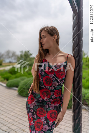 Woman floral dress park. Beautiful young woman in summer dress leaning against column looking away 132825574