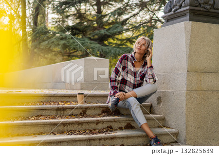 Young woman talking phone sitting park stairs autumn Young woman talking phone sitting park stairs autumn 132825639