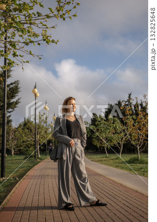 Woman, Park, Path - Woman standing on a path in a park wearing a gray suit. Woman, Park, Path - Woman standing on a path in a park wearing a gray suit. 132825648