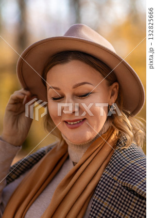 Woman Hat Autumn; Portrait, smiling woman adjusts hat outdoors during fall; golden hour lighting enhances mood. 132825666
