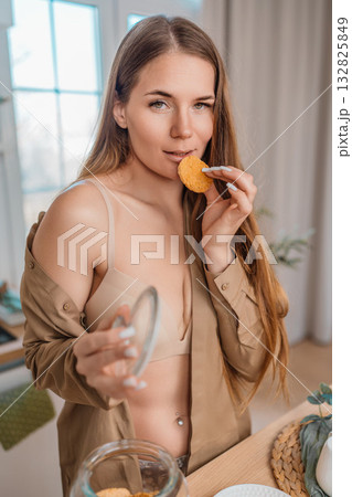 Woman, eating, cookie. Young woman casually eating a delicious snack in her cozy home. Woman, eating, cookie. Young woman casually eating a delicious snack in her cozy home. 132825849