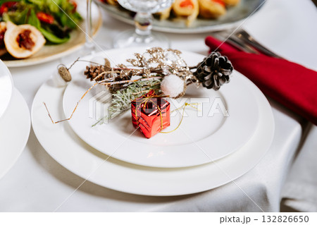 Elegant holiday table setting with festive decoration and small red gift box on plate Elegant holiday table setting with festive decoration and small red gift box on plate 132826650