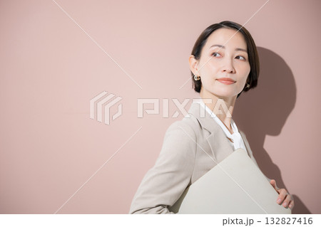 ピンクの背景でノートパソコンを持つカッコイイ女性 転職やキャリアウーマンのイメージ ピンクの背景でノートパソコンを持つカッコイイ女性 転職やキャリアウーマンのイメージ 132827416