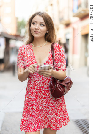 Girl in summer dress walks along street of the old town with mobile phone in her hands Girl in summer dress walks along street of the old town with mobile phone in her hands 132828201