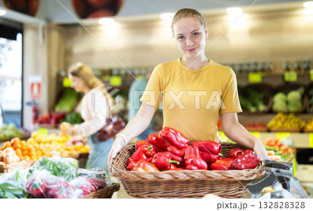 Teenage girl seller puts pepper in vegetable shop Teenage girl seller puts pepper in vegetable shop 132828328