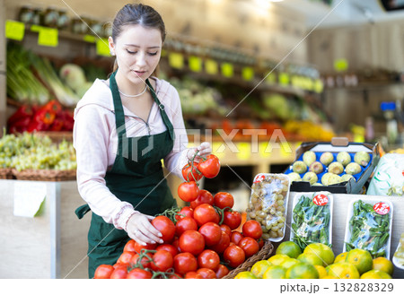 Young woman seller puts tomatoes in vegetable shop 132828329
