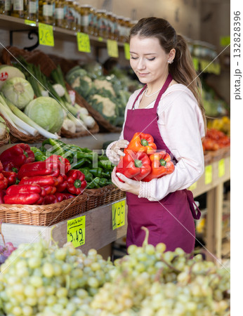 Young woman seller puts pepper in vegetable shop 132828396