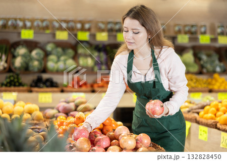 Young woman seller puts pomegranate in vegetable shop Young woman seller puts pomegranate in vegetable shop 132828450