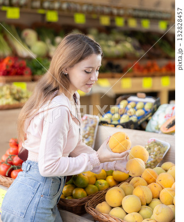 Woman chooses peaches for purchase in greengrocer shop 132828457