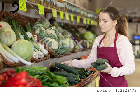 Female saleswoman laying out cucumbers Female saleswoman laying out cucumbers 132828475