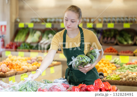 Teenage girl seller puts packaged peppers in store Teenage girl seller puts packaged peppers in store 132828491