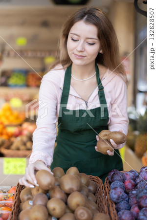 Young woman seller laying out kiwi on counter 132828507